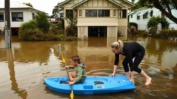 Binti Jones (right) and her son Matthew Jones 5 paddle along a flooded Bright street towards their home in Lismore. Photo: Kate Geraghty