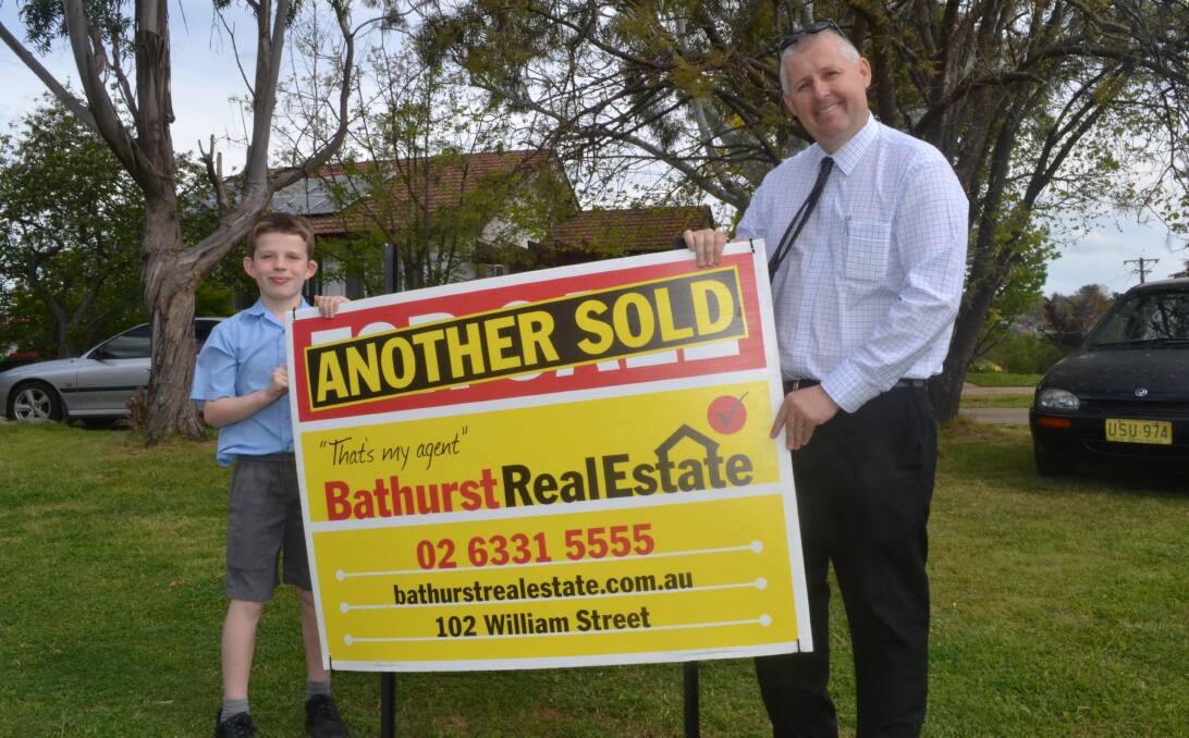 SOLD: Nathanael Boylan helps Jay Cleary, from Bathurst Real Estate, put the sold sign on his parents' property on Friday afternoon.The house was sold after only one day on the market.