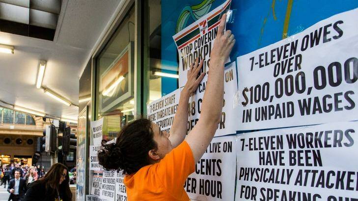 Protesters from the Young Workers Centre pin signs to the windows of a 7-Eleven store. Photo: Paul Jeffers