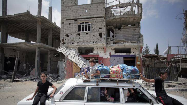 Palestinians in a car with their belongings drive past a destroyed house in Rafah's district of Shawkah in the Gaza Strip.