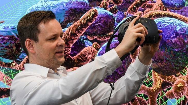 UNSW's John McGhee holds the virtual reality mask that allows you to explore inside a breast cancer cell. Mitochondria and endosomes form the backdrop. Photo: Peter Rae