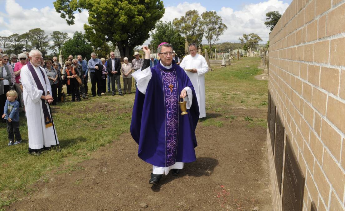 NOW AND FOREVER: Catholic Bishop Michael McKenna sprinkles holy water over the final resting place of five of Bathurst’s former Catholic bishops. Photo: CHRIS SEABROOK 	110215cburial1