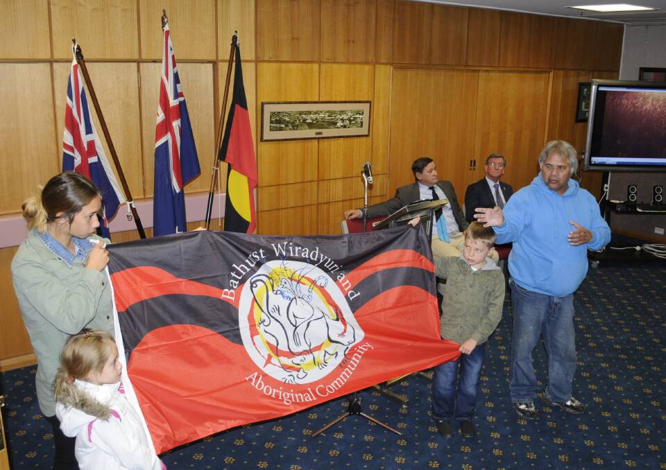 A NEW FLAG: To launch NAIDOC Week Gabby and Tilara Bugg and Bailey Crawford, hold up Bathurst’s newest flag so Wiradyuri elder Dinawan Dyirribang can explain its design. In the background are Calare MP John Cobb and mayor Gary Rush. Photo: CHRIS SEABROOK  070615cnaidoc1