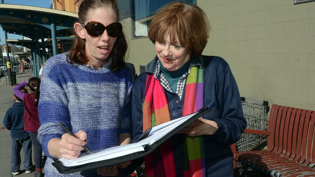 TIME FOR CHANGE: Frequent bus user Nikki Livermore signs a petition held by Bathurst Bus Community Action Group member Jenni Brackenreg, which asks the Transport Minister to address problems with the Bathurst Buslines timetable. Photo: PHILL MURRAY 070914pbus