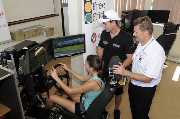 EXPERT ADVICE: Bathurst High student Sarah Tatnell, 17, is observed by V8 superstar Craig Lowndes and Keith Pappleton from Simulator Driver Safety as she takes a spin on the simulator. Photo: PHILL MURRAY 022412pcraig2