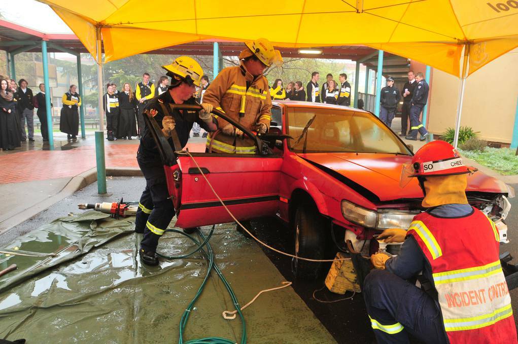 Orange Fire and Rescue NSW firefighter Mitch Crump , firefighter Mark Bell and station officer Mark Cheevers show Orange High School year 12 students what happens to the car if they end up trapped inside. Photo: JUDE KEOGH 0817carwreck3
