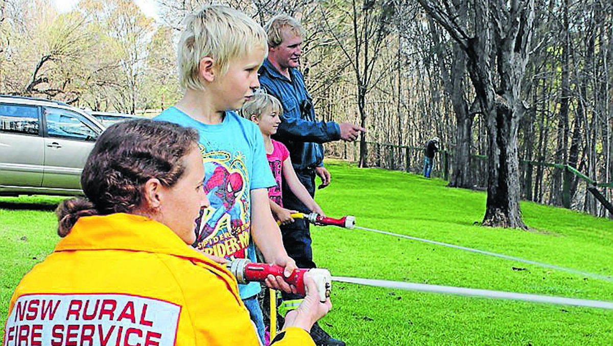 MUDGEE:  Local RFS volunteers Emily McManus and Brendon Liney (background) show youngsters Cooper and Ruby Dyke the hoses at a community engagement day at the Lawson Park markets.