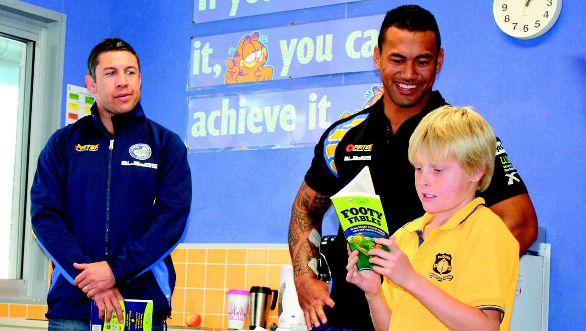 MUDGEE:Mudgee Public School student Adam Foley reads from the book ‘Footy Fables’ over Skype to players in Parramatta. Standing behind him are retired Eels captain Nathan Cayless and injured forward Taniela Lasalo.