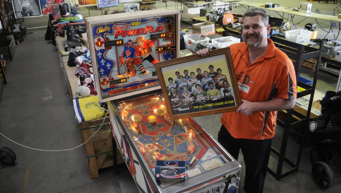 ON OFFER: Panorama Auctions director Nathan Hughes with a pinball machine  and a 1980s NSW Rugby League players poster, amongst the various items up for auction. Photo: CHRIS SEABROOK 091317cave1