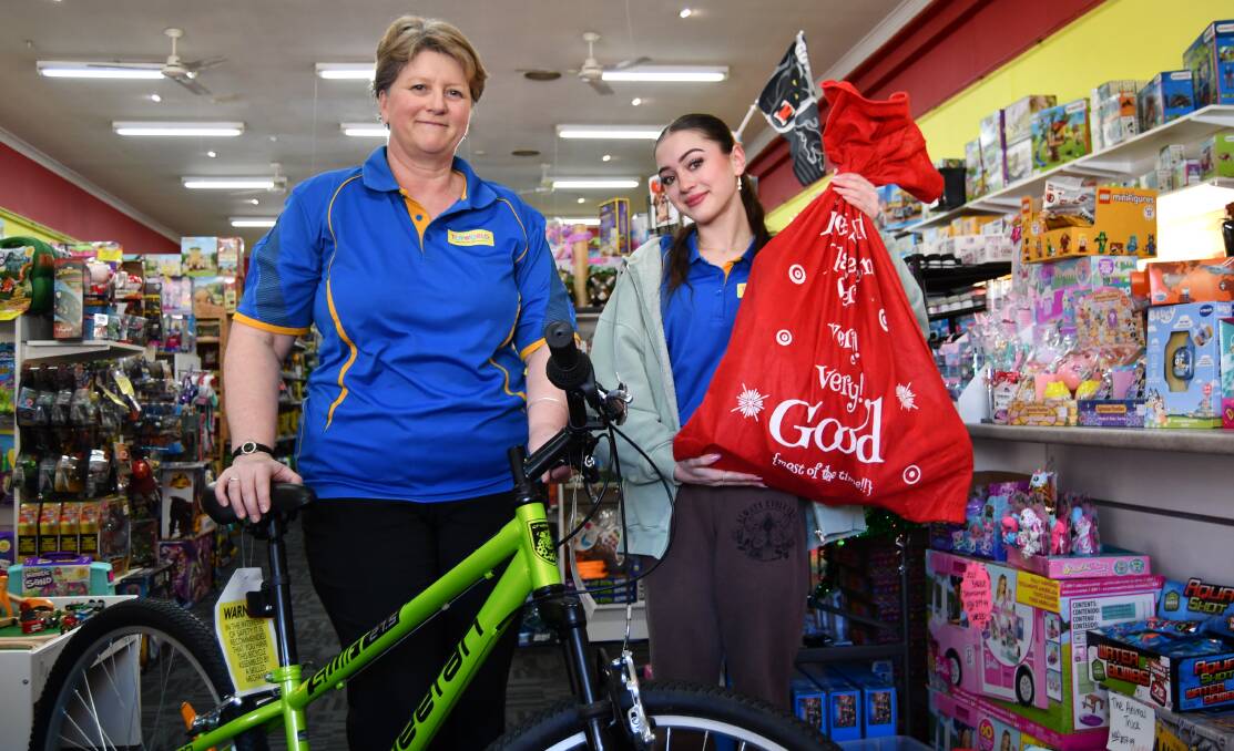 Toyworld Bathurst store assistants, Tara Laranch and Katie Brennan with a bag of donations - and a bike to be gifted - for the Christmas initiative. Picture by Jay-Anna Mobbs