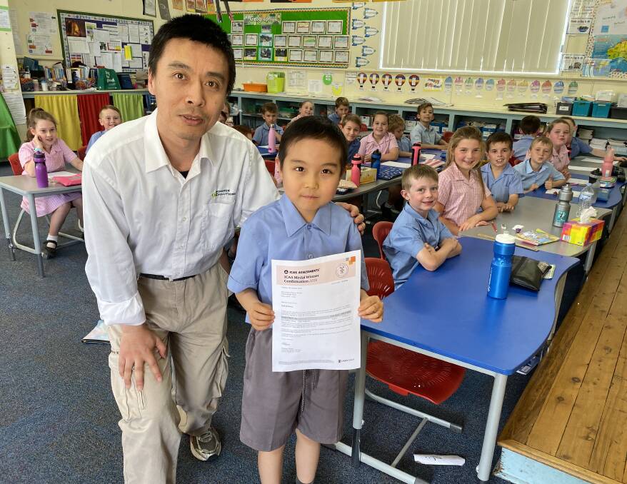 ACHIEVER: William Wang and his son Eric, who excelled in a statewide science competition, and year two students at Holy Family School.