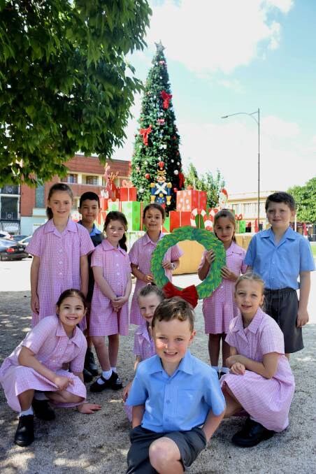 MERRY CHRISTMAS: Students from Cathedral Primary School in front of the big Christmas tree that's now in Kings Parade. Photo: RACHEL CHAMBERLAIN 113018rctree1