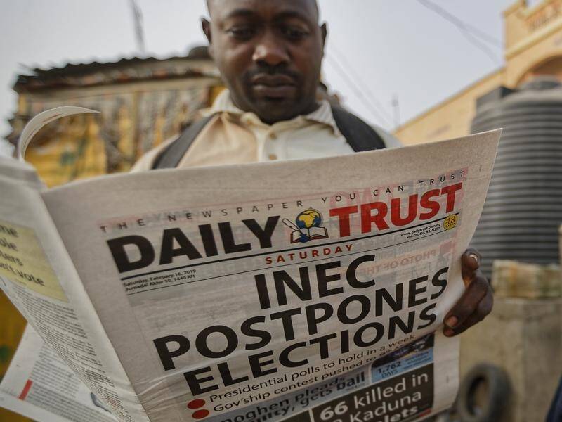 A man reads a newspaper reporting that Nigeria's presidential election has been postponed.
