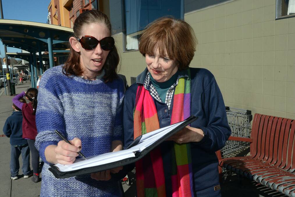 TIME FOR CHANGE: Frequent bus user Nikki Livermore signs a petition held by Bathurst Bus Community Action Group member Jenni Brackenreg, which asks the Transport Minister to address problems with the Bathurst Buslines timetable. Photo: PHILL MURRAY 	070914pbus