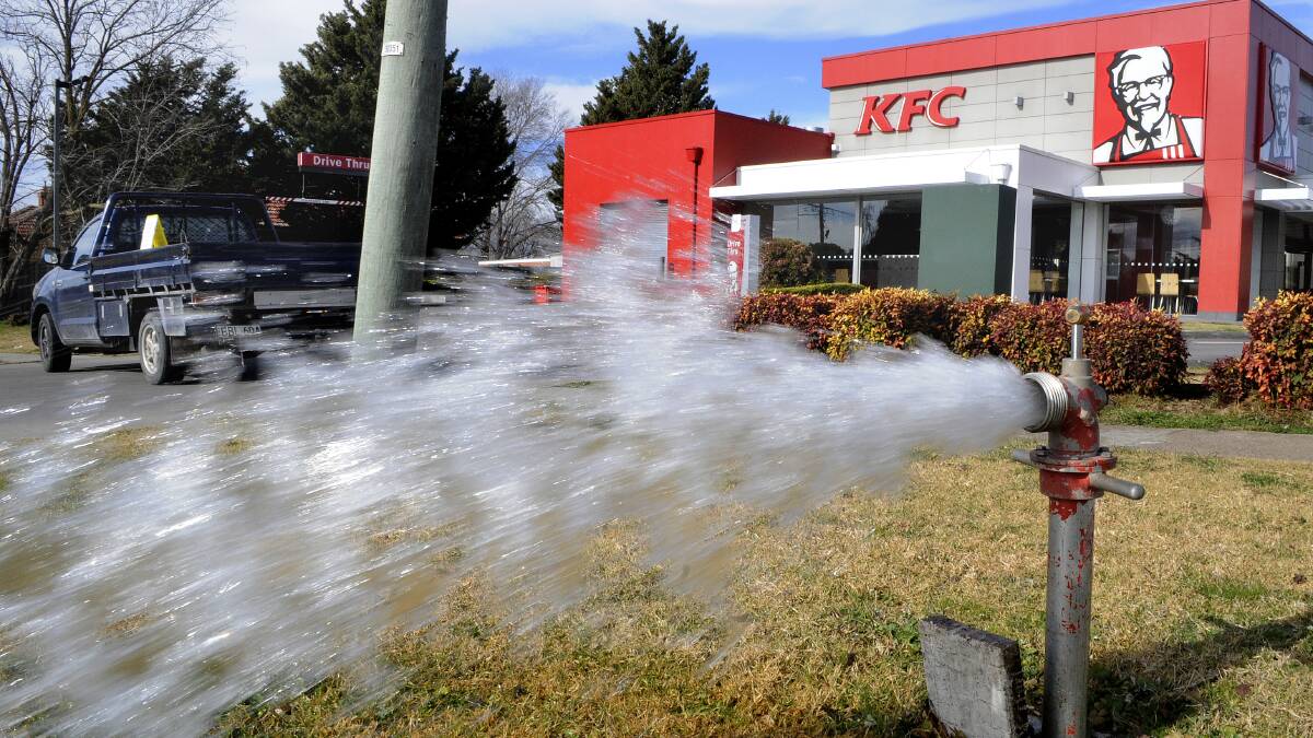 OFF THE MENU: Water gushes from a main in lower George Street on Monday as council flushes dirty water from the mains. KFC was forced to close until the water ran clear again. Photo: CHRIS SEABROOK  072114ckfc1