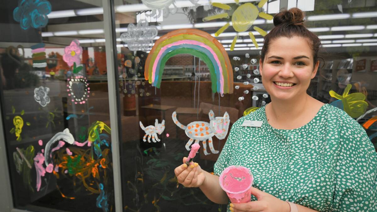 COLOURFUL: Bathurst Library programs team leader Tori Murray with a window painted at the school holidays workshop. Photo: CHRIS SEABROOK 011122cwindows1
